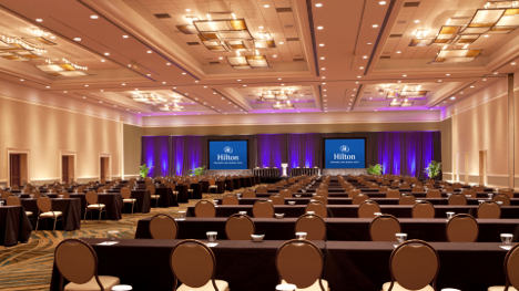 Empty hotel conference room with tables and chairs and two large monitors.