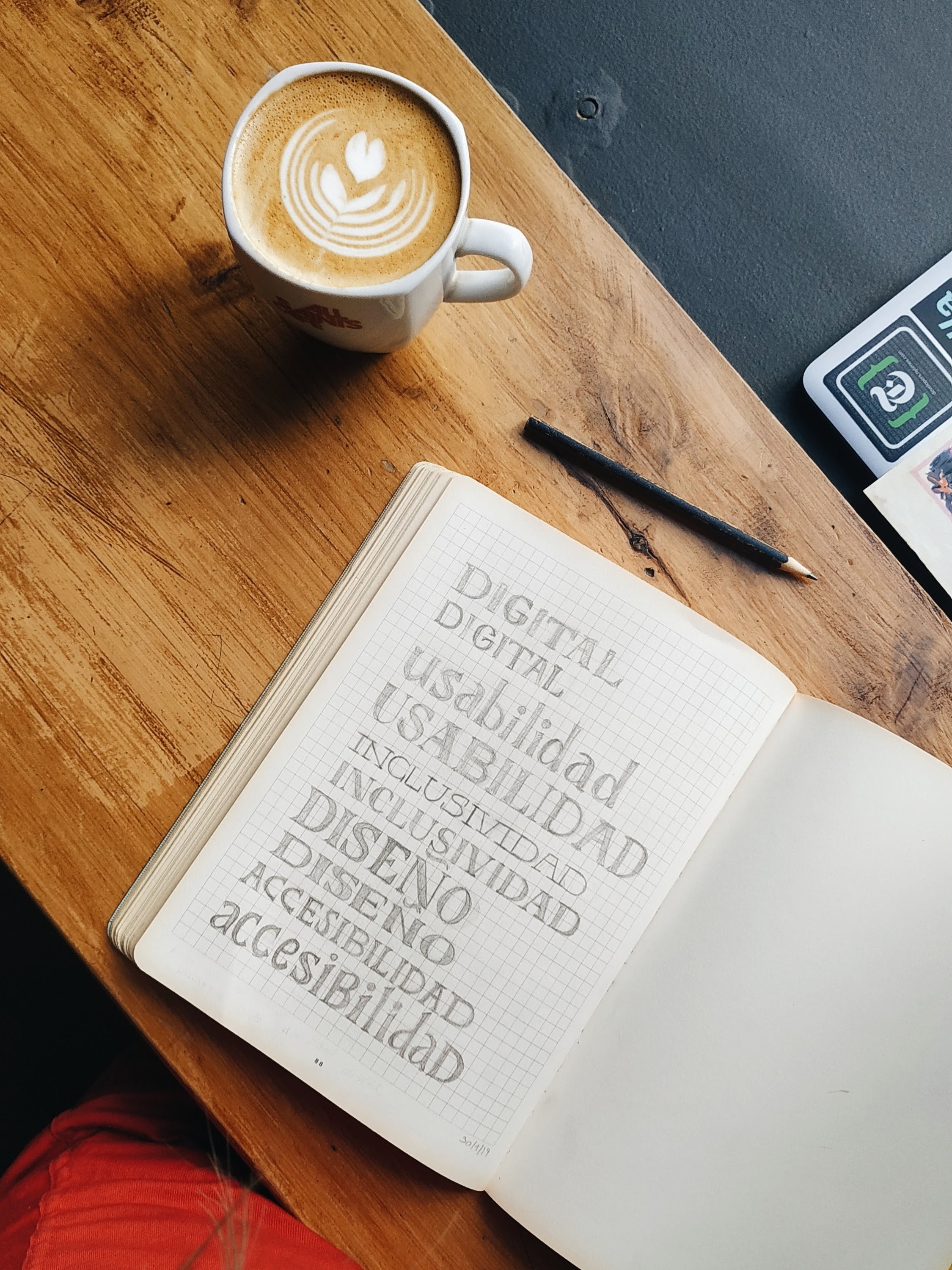 A white ceramic mug full of coffee on a wooden desk next to a notebook that says different accessibility terms.