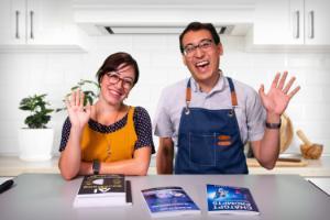 ecstatic presenters Leslie Mojeiko and Chris Sharp wearing aprons in a virtual kitchen with books about AI in front of them